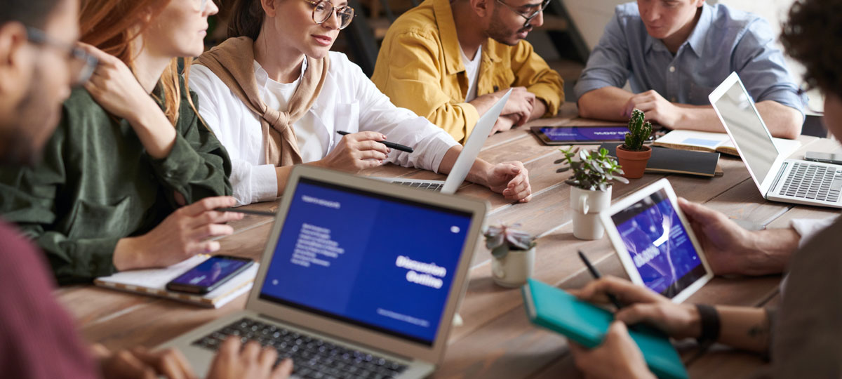 workers around an office boardroom with multiple devices and software